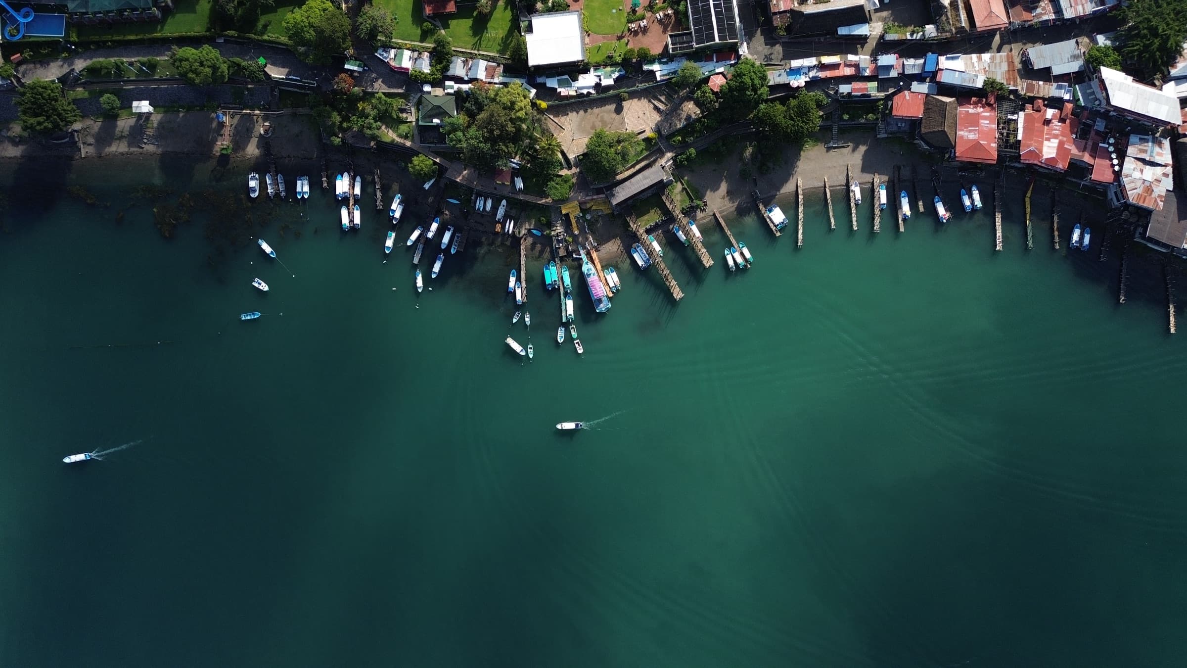 Aerial view of the Lake Atitlán shoreline, boats moored along the docks with mountains beyond