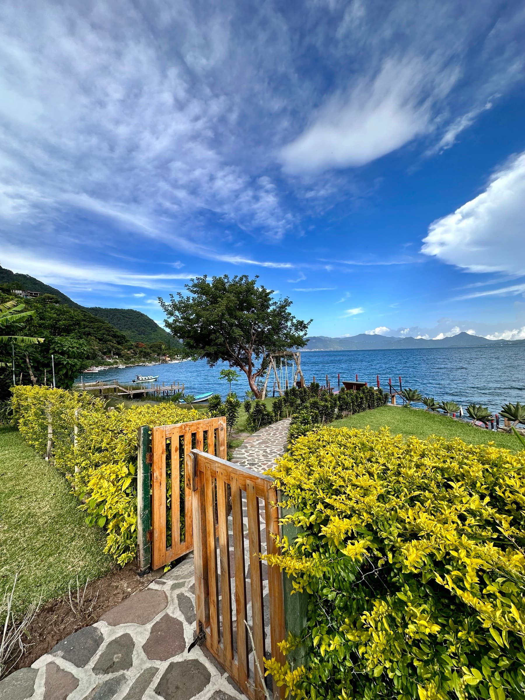 A garden gate opening onto Lake Atitlán, Guatemala, with blue sky and mountains across the water